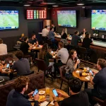 Fans engaging in live sports betting at https://ok365.br.com with smartphones and screens showing odds.