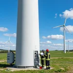 Löschwasserzisterne für Windpark in einem sonnigen Windpark-Umfeld mit Fachleuten, die Brandschutzmaßnahmen überprüfen.